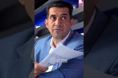 Man in blue suit holding and reading briefing papers with attentive expression at a politiska ekonomiska event