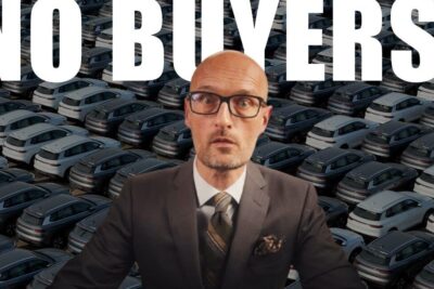 Surprised bald man in a suit and glasses stands before rows of parked cars and large 'NO BUYERS!' text, emphasizing potentielle fordele.