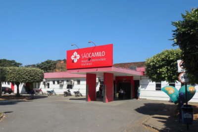 Front entrance of São Camilo hospital with red canopy, parked motorcycles and visitors, a visual call to preservar a historia e a cultura dos monumentos historicos contra a exploracao turistica