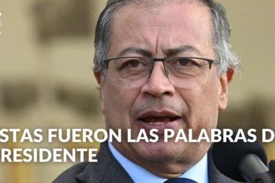 Close-up of a man in glasses speaking into a microphone with a televised headline and news logo, proceso paz 2