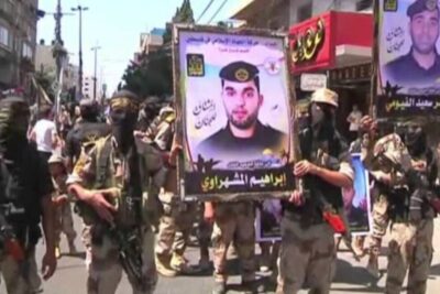 Armed masked fighters marching in a city street holding large framed portrait posters, processo paz 2