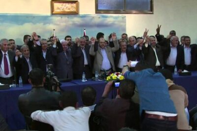 Group of delegates in suits standing behind a table and raising joined hands at processo paz 4