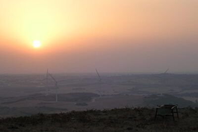 Hilltop sunset with wind turbines and a solitary chair suggesting productos practicas for outdoor relaxation.