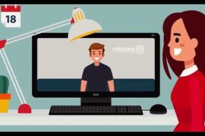 Smiling woman at a desk watching a presenter on a desktop monitor during a video call, produtos servicos 1