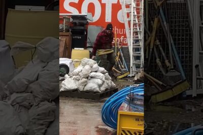 Worker coiling a hose beside stacked sandbags, ladders and tools to prove concrete site preparedness.