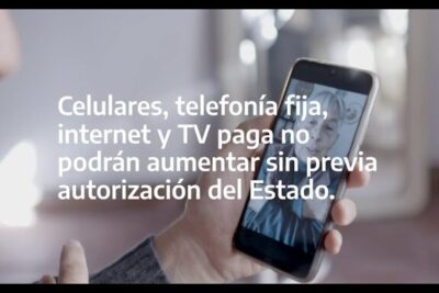 Hand holding a smartphone displaying a video call with overlaid regulatory text about service price increases — publicos esenciales 1