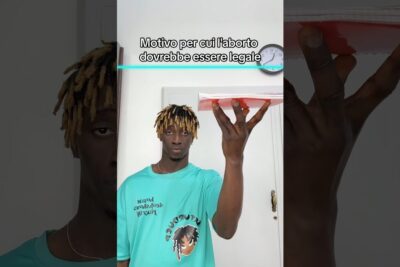 Individual in teal shirt holds a red object beneath an Italian on-screen headline about ragioni laborto.