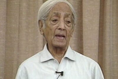 Elderly man speaking with a lapel microphone against a curtain backdrop, reazioni divisive 1