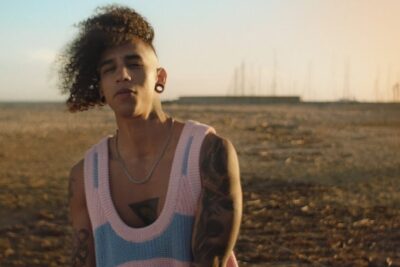 Portrait of a tattooed person on a sandy beach at golden hour wearing a pastel knit top for red social 5.