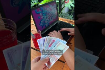 Person holding a fan of colorful banknotes while another types on a laptop, illustrating reforma laboral 1
