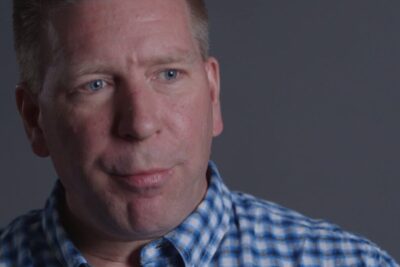 Close-up portrait of a man in a blue checked shirt thoughtfully considering reformerade arbetsmarknaden.