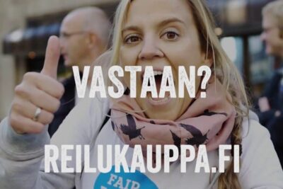 Enthusiastic person giving a thumbs up at a fair trade rally with bold overlay text and a campaign badge, reilun kaupan 1