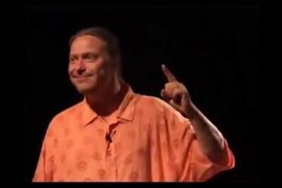 Smiling presenter on a dark stage raising a finger to emphasize relativisme culturel
