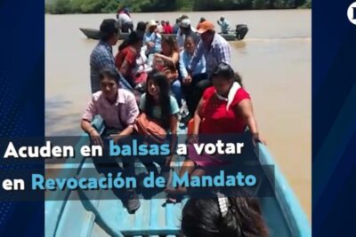 Group of people seated in a narrow blue boat on a muddy river heading to vote in revocation mandat 1
