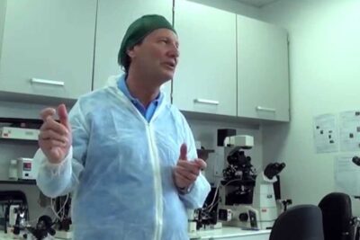 A lab professional in protective gown gestures beside microscopes and equipment in an embryology room for riproduzione assistita 2.