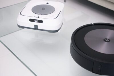 Black circular and white rectangular robotit voivat 1 robotic vacuums on a glass tabletop.