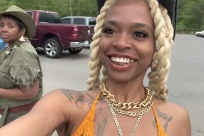 Smiling attendee selfie with braided blonde hair, gold chains and tattoos in a rodeo ar parking lot