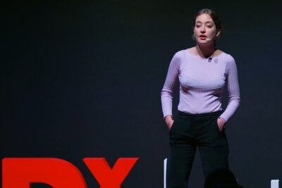 Woman speaker on a dark stage with headset microphone presenting on salute mentale.