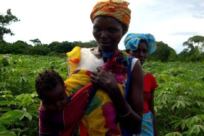 Two women and a baby in a green crop field wearing colorful headwraps, samfund 4.