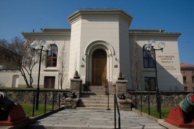 Cream-colored classical building entrance with arched doorway, stone steps, globe lamps and samfund 9