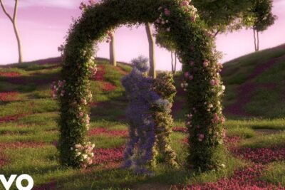 Two floral sculptures shaped like embracing figures beneath a rose-covered arch in a pink meadow, san valentin 1.