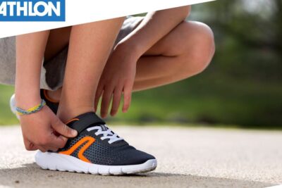 Child tying black and orange scarpe bambini with white sole on pavement
