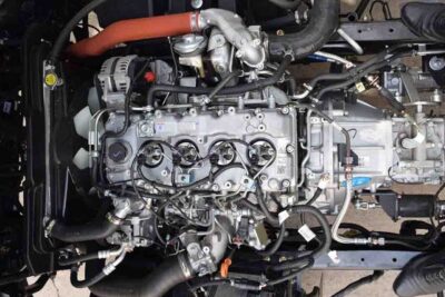 Top-down view of a turbocharged four-cylinder engine with visible alternator, hoses, and wiring harness, se voi