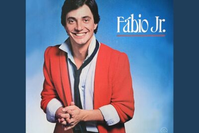 Smiling man in a red jacket with a loosened tie against a blue backdrop, representing seres humanos