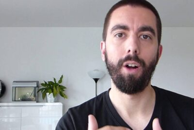 Bearded presenter gesturing towards camera in a home office setting while discussing services publics and municipal programs