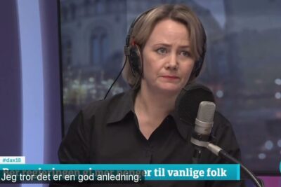 Woman in radio studio wearing headphones at a microphone discussing skatter avgifter.