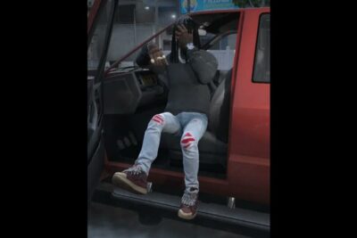 Seated person on a truck step wearing burgundy sko babyer sneakers with patterned laces and ripped light jeans.
