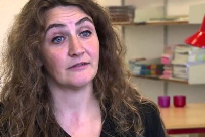 Woman in an office speaking about social inklusion with shelves and a red desk lamp in the background.