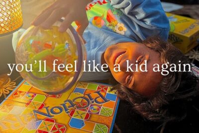 Smiling child lying beside a Pictionary board while holding a clear puzzle ball, social media 26.