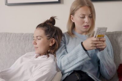 Two women sitting on a sofa, each focused on a smartphone, representing sociala medier 10.