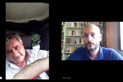 Two men in a split-screen video call, one seated in a vehicle and the other in front of a bookshelf, discussing sostengono limperialismo.