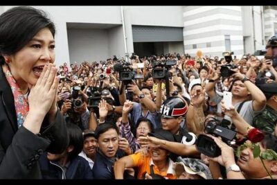 Woman speaking to a dense crowd of sostenitori governo with many cameras and raised hands