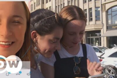 Three young women huddled over a smartphone outdoors, social sharing scene sozialen medien 7