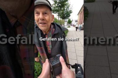 Candid close-up of an elderly man smiling on a sidewalk as a photographer holds a camera, a spontanen generation street moment