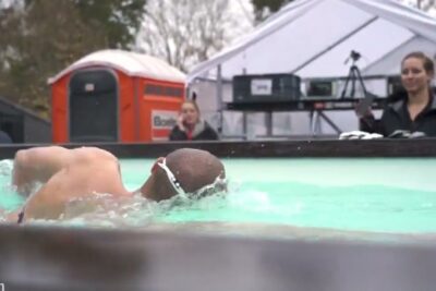 A swimmer performing strom schwimmen in an outdoor pool wearing goggles and executing a freestyle stroke.