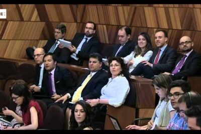 Seated group in a wood-paneled chamber appearing to discuss subir impuestos.