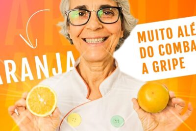 Smiling older woman in a white chef coat holding a halved orange and a whole orange promoting suco laranja 1