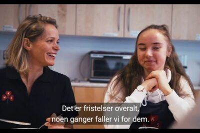 An adult and a teenager smiling while sharing food at a kitchen table, sunt kosthold 1