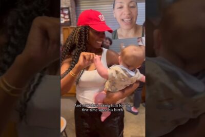Smiling woman holds a newborn in a joyful surrogati graviditet reunion while another woman watches on a video call