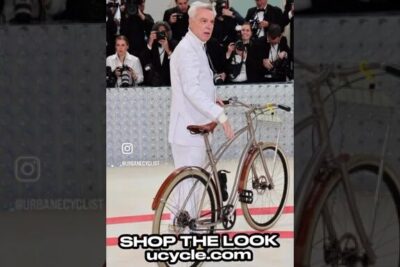 Person in a white suit pushing a classic city bicycle with leather saddle and fenders on a runway, sykler byene.