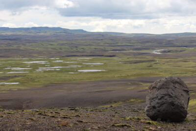 Expansive highland plateau with a solitary boulder and scattered shallow ponds, tabacon laki.