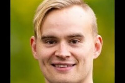 Smiling young man portrait against a soft green background illustrating taloudelliset edut.