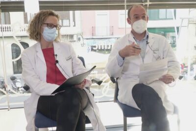Two masked clinicians in white coats seated with documents discussing tasa curacion 1