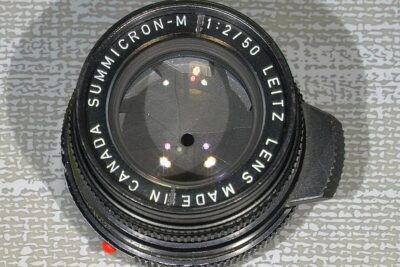 Close-up of a vintage camera lens showing aperture blades, glass reflections and a threaded metal mount, teflon gjengelasning 1.