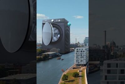 A giant washing machine suspended above a city canal as a surreal installation showcasing teknologiske innovasjoner.