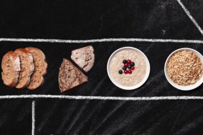 Assortment of whole grain breads, a bowl of porridge with berries and a bowl of oats for terveellisen ruokavalion